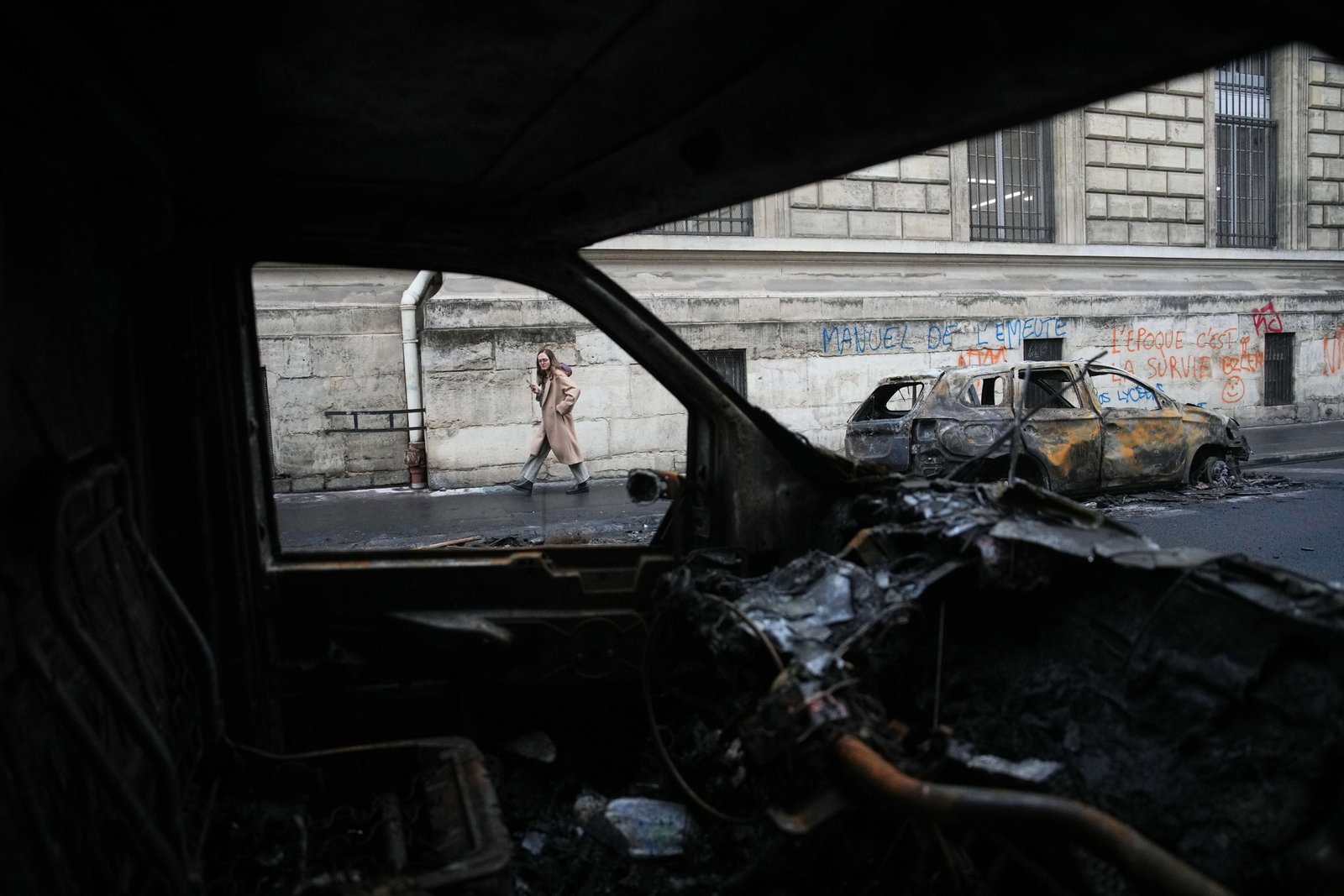 A woman walks past burned-out cars after a quiet night Monday under curfew, the first since weekend protests over the cost of living turned into rioting and looting across France, in Paris, Tuesday, Oct. 20, 2026.