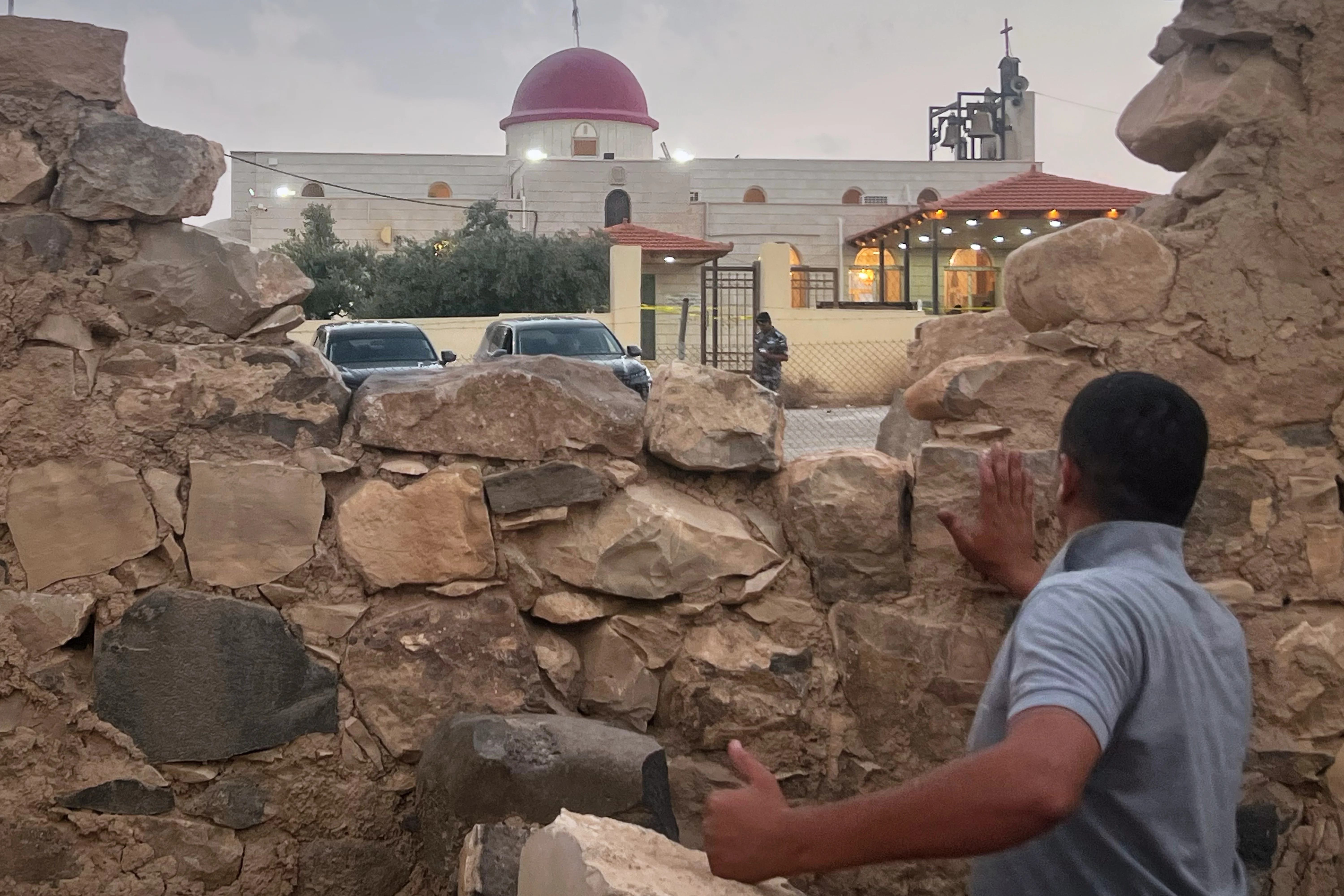 A man looks through a gap in a stone wall toward a Greek Orthodox church where gunmen opened fire during a funeral hours earlier in Hamoud village, in Jordan