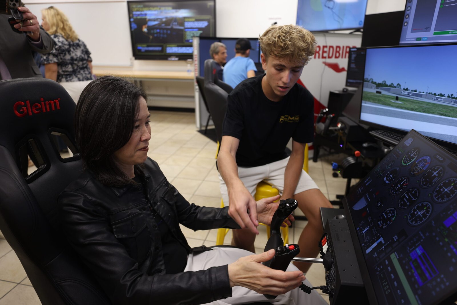 Elaine Ho sitting in a chair with her hands on controller with a student helping set up the simulator
