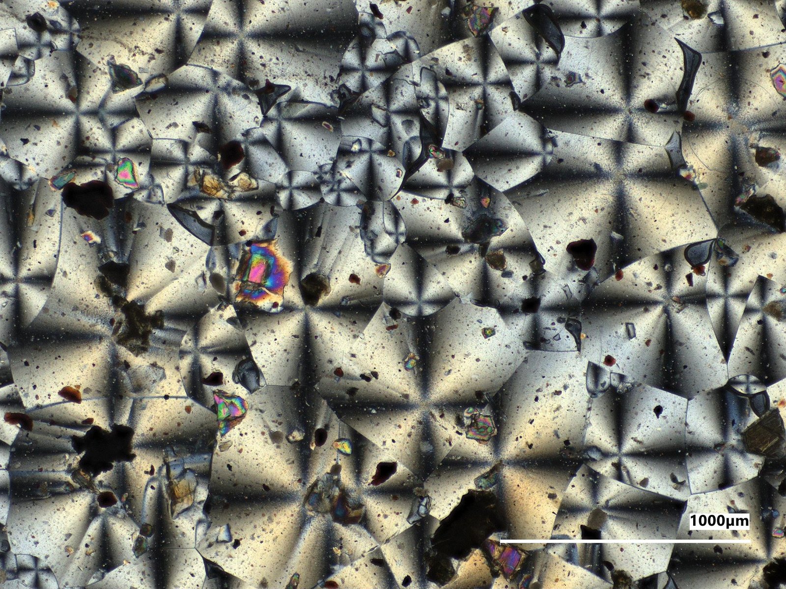 A microscopic view of the kaleidoscope-like crystal structures of two NASA-made material samples, a gray sample on the left and a reddish sample on the right.